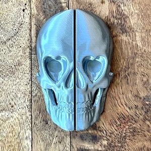 May include: A pair of silver skull bookends with heart-shaped eyes. The bookends are made of a smooth, matte material and are a unique and decorative addition to any bookshelf.