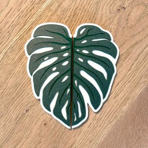 Op de afbeelding: Een groene monstera-bladvormige deurknop met een witte omtrek.