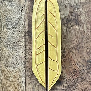 May include: A pair of gold-colored metal door handles shaped like a leaf. The handles are separated and ready to be installed.