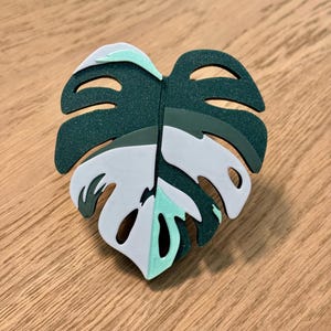 May include: A white and green monstera leaf shaped wall decor with a textured surface.