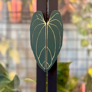 May include: A dark green leaf-shaped door handle with gold veins. The handle is mounted on a black door.