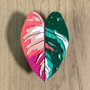 May include: A heart-shaped leaf with a pink, white, and green color scheme. The leaf is made of a textured material and has a 3D effect.