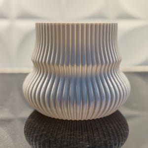 May include: A white ceramic planter with a ribbed design. The planter has a rounded base and a slightly flared top.