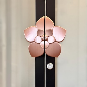 May include: A rose gold flower-shaped door handle with a keyhole on a black door.