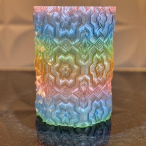 May include: A rainbow-colored cylindrical vase with a geometric pattern. The vase is made of a translucent material and has a glossy finish.