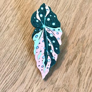 May include: A green, pink, and white leaf-shaped brooch with white polka dots. The brooch is made of a textured material and has a glossy finish.