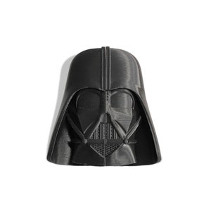 May include: A black 3D printed Darth Vader bust. The bust is detailed and shows the iconic helmet and mask of the Star Wars character.