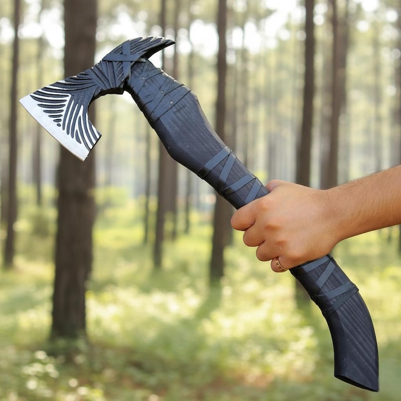 May include: A dark axe with a silver blade and a black handle, held against a backdrop of trees. The axe head has a distinctive white and black striped pattern, and the handle is wrapped in dark bands.