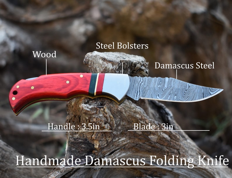 May include: A handmade Damascus folding knife featuring a red wood handle with brass pins, steel bolsters, and a patterned Damascus steel blade. The handle measures 3.5 inches and the blade measures 3 inches, as labeled in the image text.