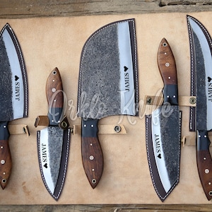 May include: A set of five handcrafted knives with wooden handles and dark blades, displayed in a leather roll. Each knife has the name "JAMES" and a heart symbol. The knives are of varying sizes and shapes.