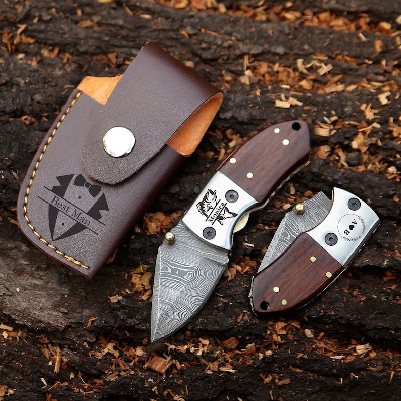 May include: A set of three pocket knives with wooden handles and Damascus steel blades. One knife is open, one is closed, and the third is in a brown leather case with "Best Man" printed on it. The knives have silver accents.