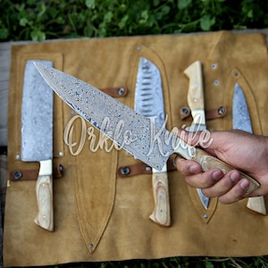 May include: A collection of knives with patterned blades and wooden handles displayed on a brown leather roll. One knife is held in a hand. The text "Orklo Knife" is visible on the image.