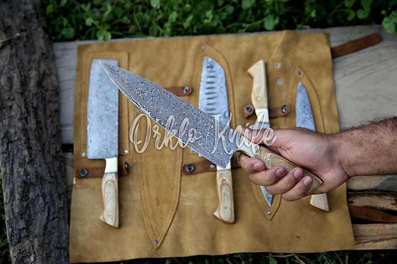 May include: A collection of knives with patterned blades and wooden handles displayed on a brown leather roll. One knife is held in a hand. The text "Orklo Knife" is visible on the image.
