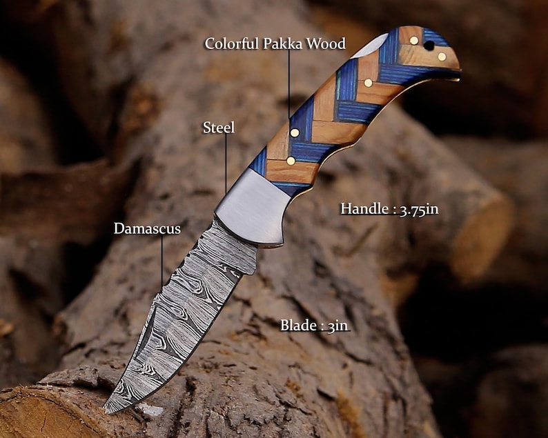 May include: A folding knife with a 3-inch Damascus steel blade and a 3.75-inch handle made of colorful Pakka wood in a blue and brown woven pattern. The knife features a steel bolster and brass pins, with text labels identifying the blade, steel, handle, and wood.