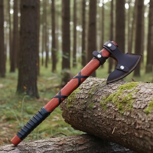 May include: A traditional axe with a dark leather blade cover and a wooden handle. The handle is wrapped with black leather and has black cross-shaped details. The axe is displayed on a log in a forest.