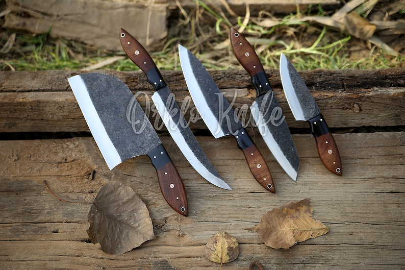 May include: A collection of five handcrafted knives with dark, textured blades and wooden handles. The handles are a rich brown with black accents. The knives are arranged on a rustic wooden surface, showcasing their unique design.