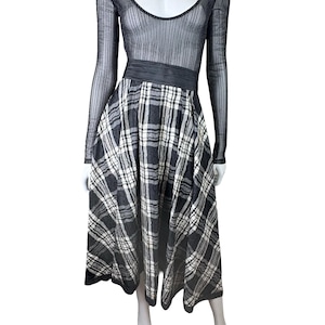 May include: A black and white plaid dress on a mannequin. The dress features a sheer, long-sleeved top and a wide black waistband. The skirt is a full, midi-length plaid design.
