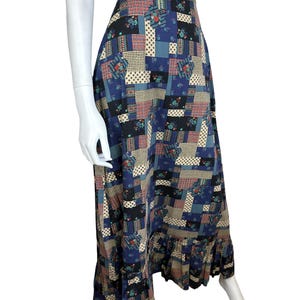 May include: A long patchwork skirt with a high waist and a ruffled hem. The skirt features a variety of patterned squares in shades of blue, beige, red, and green. The skirt is displayed on a mannequin.