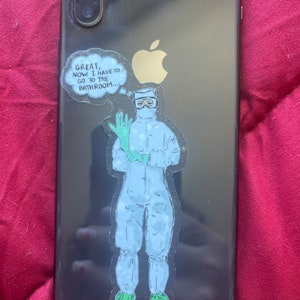 Puede incluir: Un iPhone negro con un logotipo de Apple blanco y una pegatina de un personaje de dibujos animados con un traje blanco de protección con un globo de pensamiento que dice "Genial, ahora tengo que ir al baño..."