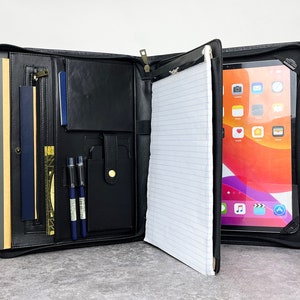 May include: Black leather portfolio with a built-in tablet holder, a zippered pocket, and a notepad. The portfolio is open and the tablet is showing a home screen with various apps.
