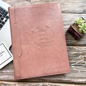 May include: A dusky pink leather portfolio with the words "school social worker" embossed in a floral wreath. A laptop and a small square card that says "Best Wishes for you" are next to the portfolio. A small succulent plant in a decorative pot is also in the image.