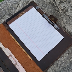 May include: A brown leather portfolio with a notepad and pen. The notepad has the word "Veritas" printed on the cover.