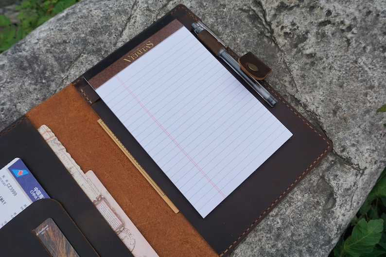 May include: A brown leather portfolio with a notepad and pen. The notepad has the word "Veritas" printed on the cover.