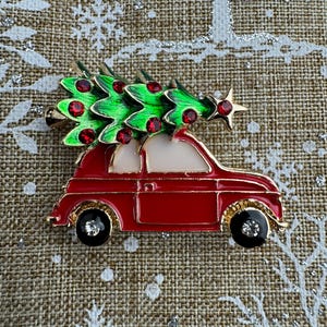 Może przedstawiać: Czerwony samochód z zielonym drzewem bożonarodzeniowym na dachu. Samochód ma złote wykończenia i czarne koła z cyrkoniami. Drzewo jest ozdobione czerwonymi ozdobami i złotą gwiazdą na szczycie.