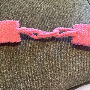 May include: Pink crocheted wrist warmers connected by a chain of crocheted loops.