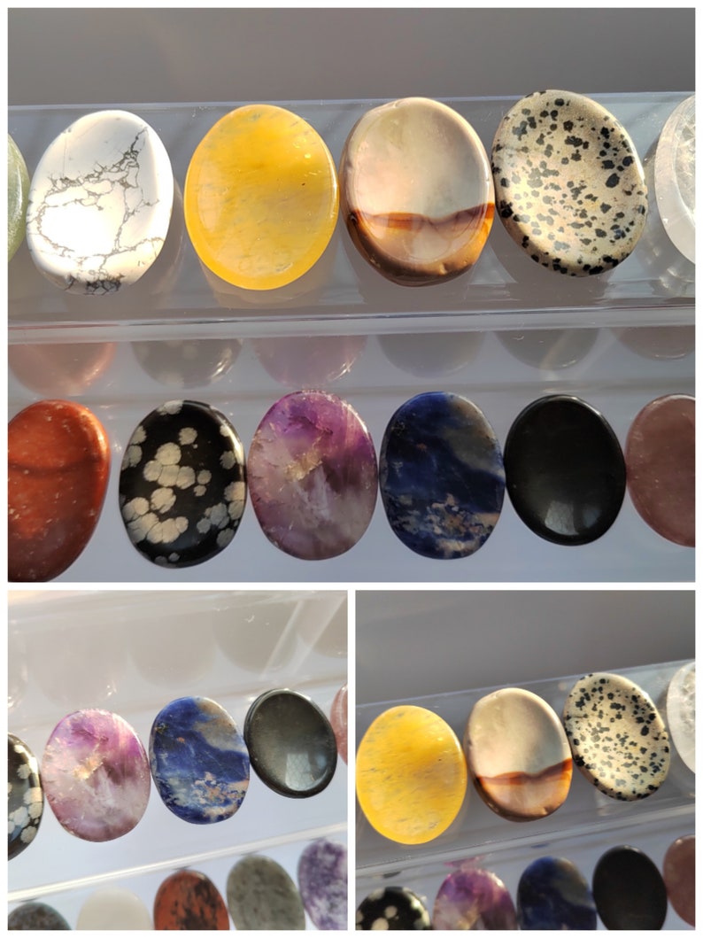 Pu&ograve; includere: Una collezione di pietre ovali levigate in vari colori e motivi, tra cui bianco, giallo, marrone, nero, viola, blu e rosso. Le pietre sono disposte in file su una superficie trasparente.