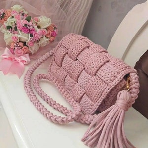 May include: A pink crocheted handbag with a long tassel. The bag has a woven design and a gold clasp.
