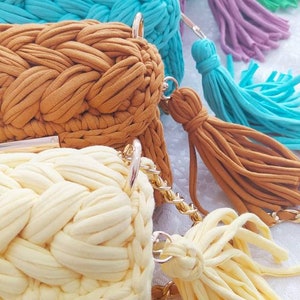 K&ouml;nnte beinhalten: F&uuml;nf geh&auml;kelte Taschen mit Quasten in verschiedenen Farben, darunter Gr&uuml;n, Lila, Blau, Braun und Gelb. Die Taschen sind mit einem geflochtenen Muster gearbeitet und haben goldfarbene Metallverschl&uuml;sse.