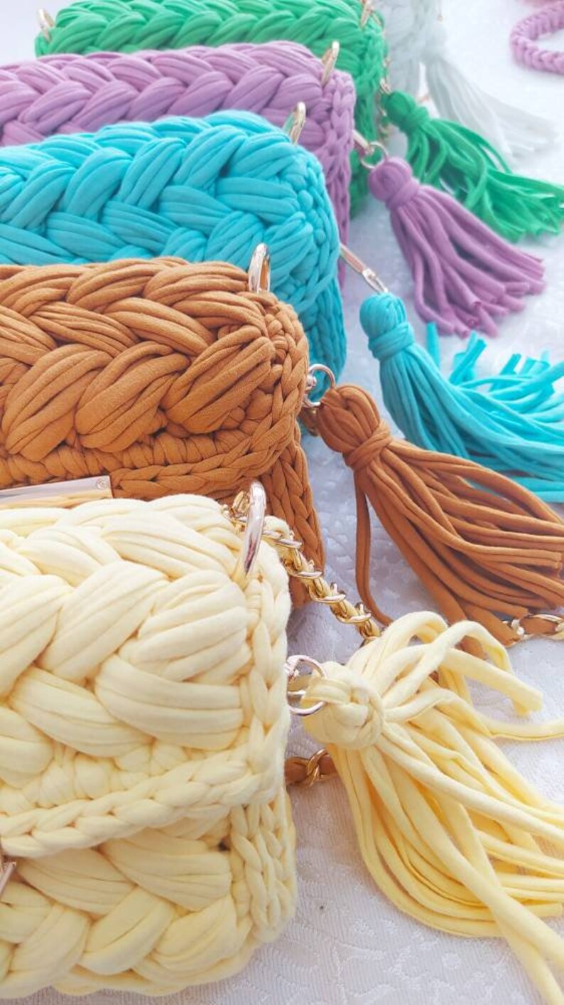 K&ouml;nnte beinhalten: F&uuml;nf geh&auml;kelte Taschen mit Quasten in verschiedenen Farben, darunter Gr&uuml;n, Lila, Blau, Braun und Gelb. Die Taschen sind mit einem geflochtenen Muster gearbeitet und haben goldfarbene Metallverschl&uuml;sse.