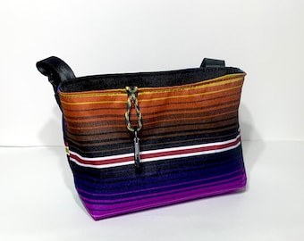 May include: A small, black, striped bag with a brown, orange, and yellow striped pattern. The bag has a black strap and a drawstring closure.