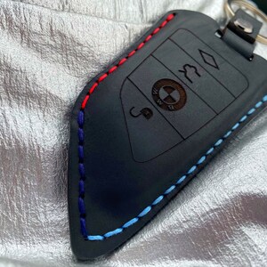 May include: Black leather key fob with blue, red, and white stitching. The fob has a BMW logo and four buttons.