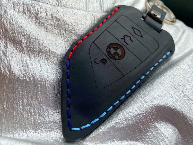 May include: Black leather key fob with blue, red, and white stitching. The fob has a BMW logo and four buttons.
