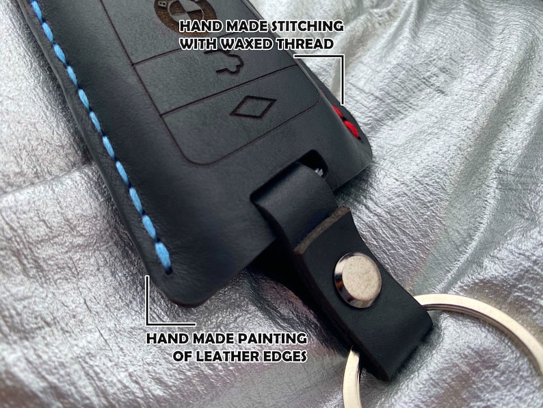 May include: Black leather key fob with blue stitching and a silver key ring. The fob has a hand-painted edge and the text "HAND MADE STITCHING WITH WAXED THREAD" is written on the top.