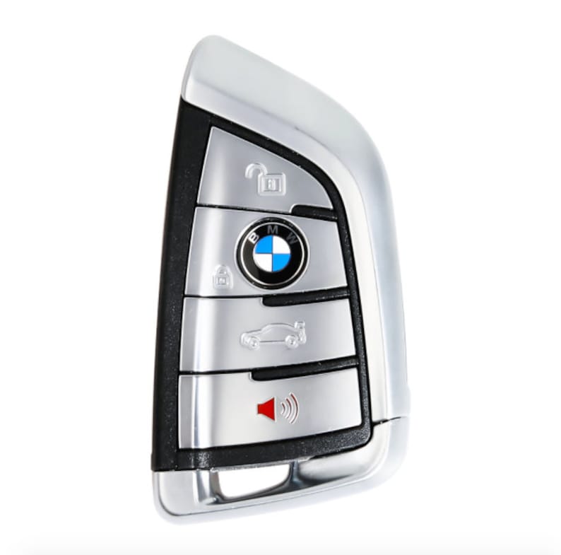 May include: A silver car key with a black button panel. The key has a BMW logo and buttons for locking, unlocking, trunk release, and panic.