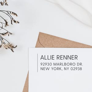 May include: A white card with black text that reads "Allie Renner", "92930 Marlboro Dr.", and "New York, NY 02938". The card is on top of a brown envelope.