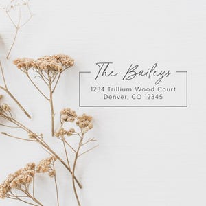 May include: A white background with the text "The Baileys" in elegant script above an address: 1234 Trillium Wood Court, Denver, CO 12345. Dried floral stems with beige blossoms are arranged around the text.