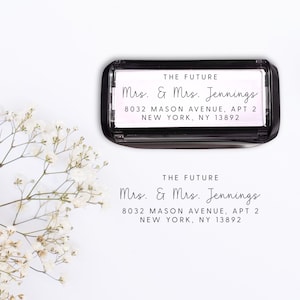 May include: A black rectangular stamp with the text "THE FUTURE" and "Mrs. & Mrs. Jennings" along with an address. The stamp is displayed on a white background with a sprig of white flowers.