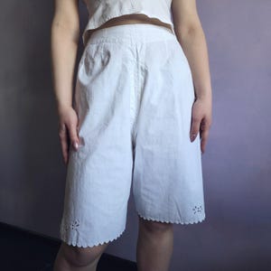 May include: White vintage bloomers with a high waist and knee-length hem. The bloomers feature a scalloped edge with floral cutouts at the hem. The fabric appears to be a lightweight cotton or linen.