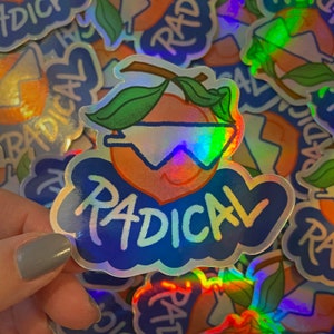 May include: A holographic sticker featuring a peach wearing sunglasses and the word "RADICAL" in a blue cloud. The peach has green leaves and a stem.