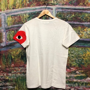 Peut inclure: T-shirt blanc avec un motif d'&oelig;il rouge sur la manche gauche.
