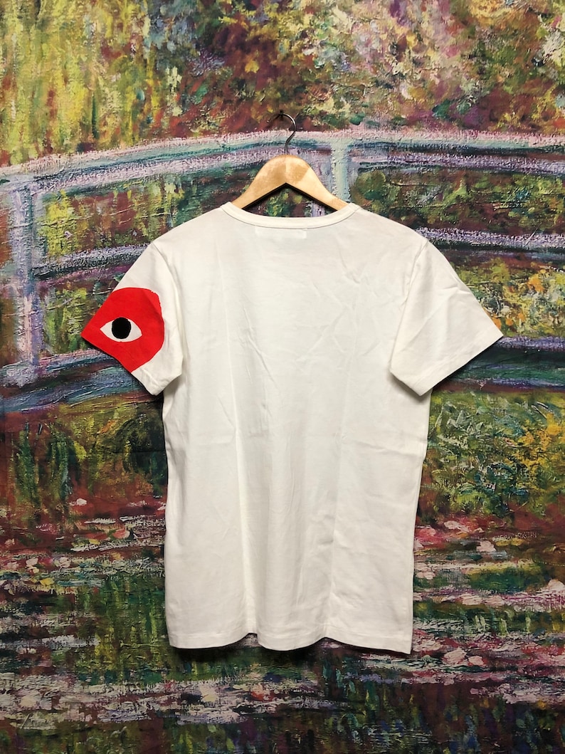 Peut inclure: T-shirt blanc avec un motif d'&oelig;il rouge sur la manche gauche.
