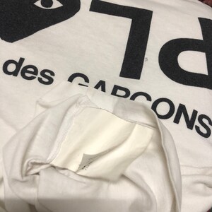 Puede incluir: Camiseta blanca con un coraz&oacute;n negro con ojos y el texto "PLAY" y "des GARCONS" impreso en ella.