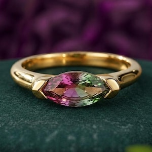Può includere: Un anello d'oro con una gemma a taglio marquise. La gemma presenta una sfumatura di colori, tra cui rosa, verde e arancione. La fascia dell'anello è in oro lucido e l'incastonatura ha un design unico.