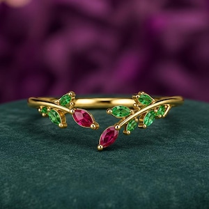 May include: A gold open-style ring featuring a branch motif adorned with marquise-cut green stones representing leaves and two vibrant red marquise-cut stones acting as focal points, creating a delicate botanical design on a polished gold band.