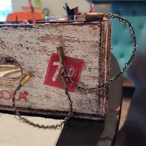 May include: A wooden crate with white paint and a red label that says "7 Up".  A silver chain is attached to the crate with brass bullet casings.
