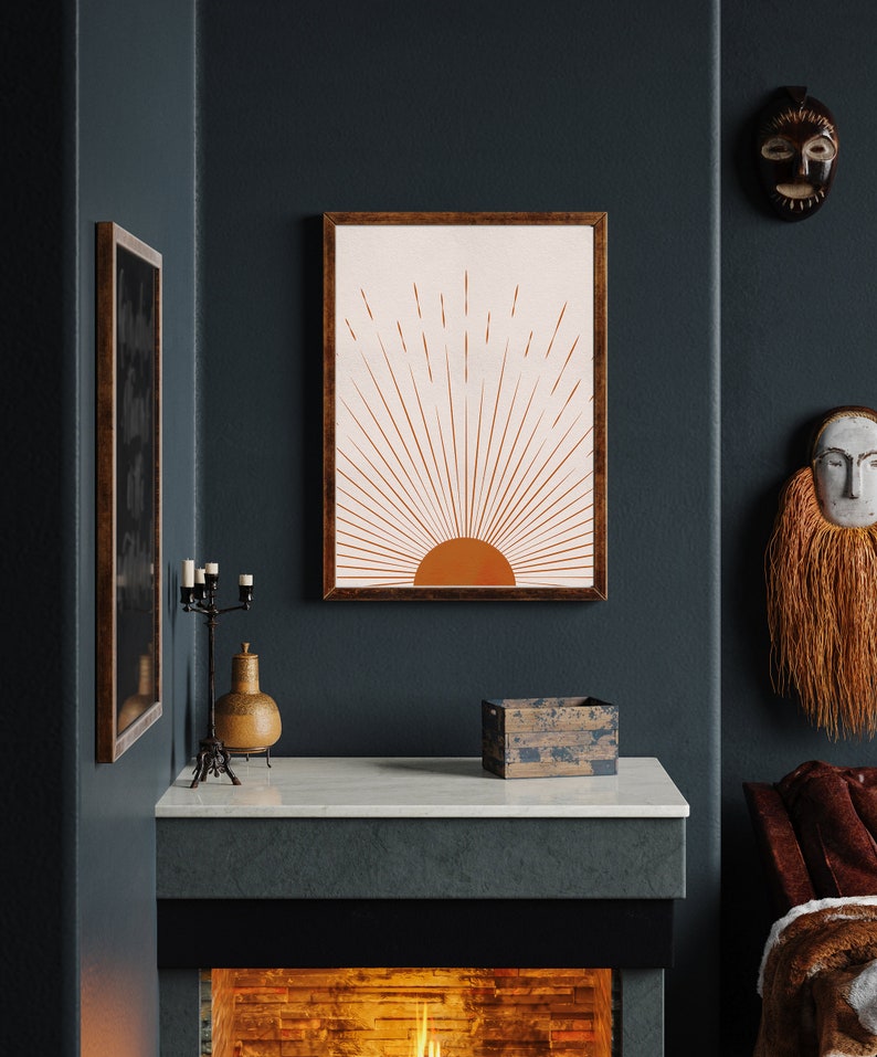 May include: A framed art print featuring a minimalist sunrise design in shades of orange and cream. The artwork is displayed on a dark teal wall, alongside other decorative items, including a candle holder and a wooden box. The overall aesthetic is warm and inviting.
